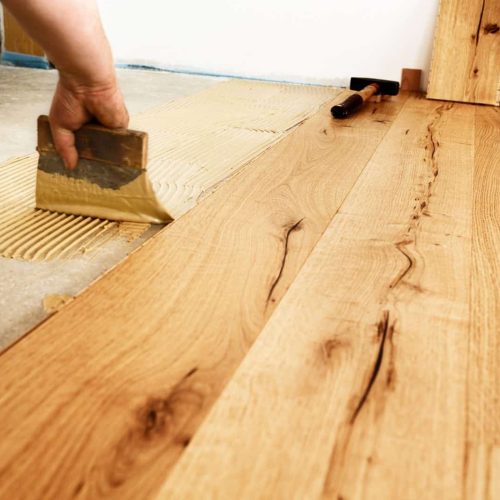 Man applying glue for laying finished parquet flooring, close-up